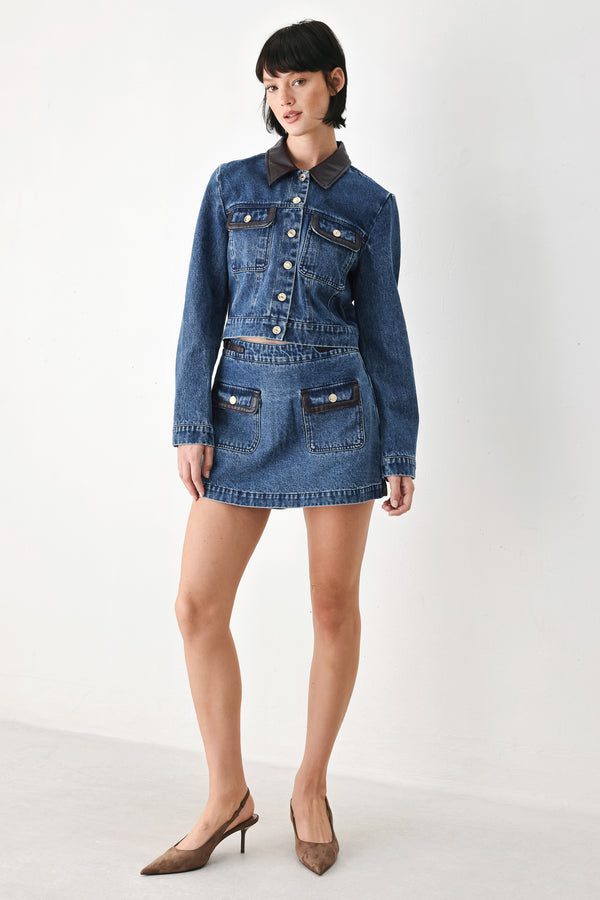 A model wearing a blue denim mini skort with dark brown leather accents on the waistband and pocket flaps | FREEMARKET
