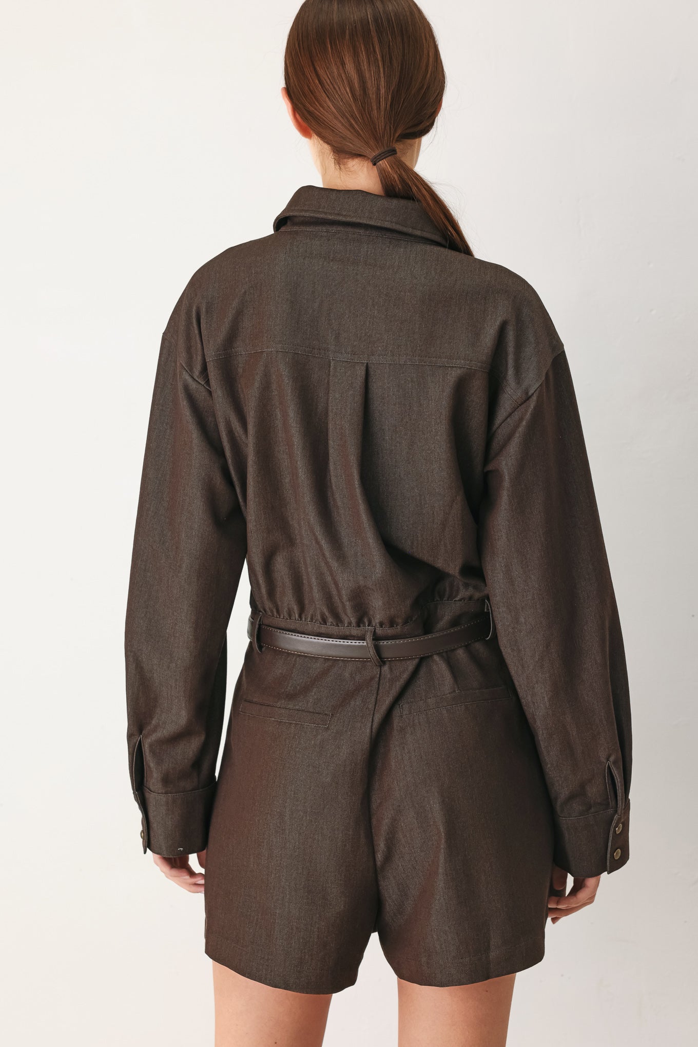Woman wearing a brown woven romper featuring front button zipper closure, pockets, long sleeves and contrasting belt | FREEMARKET