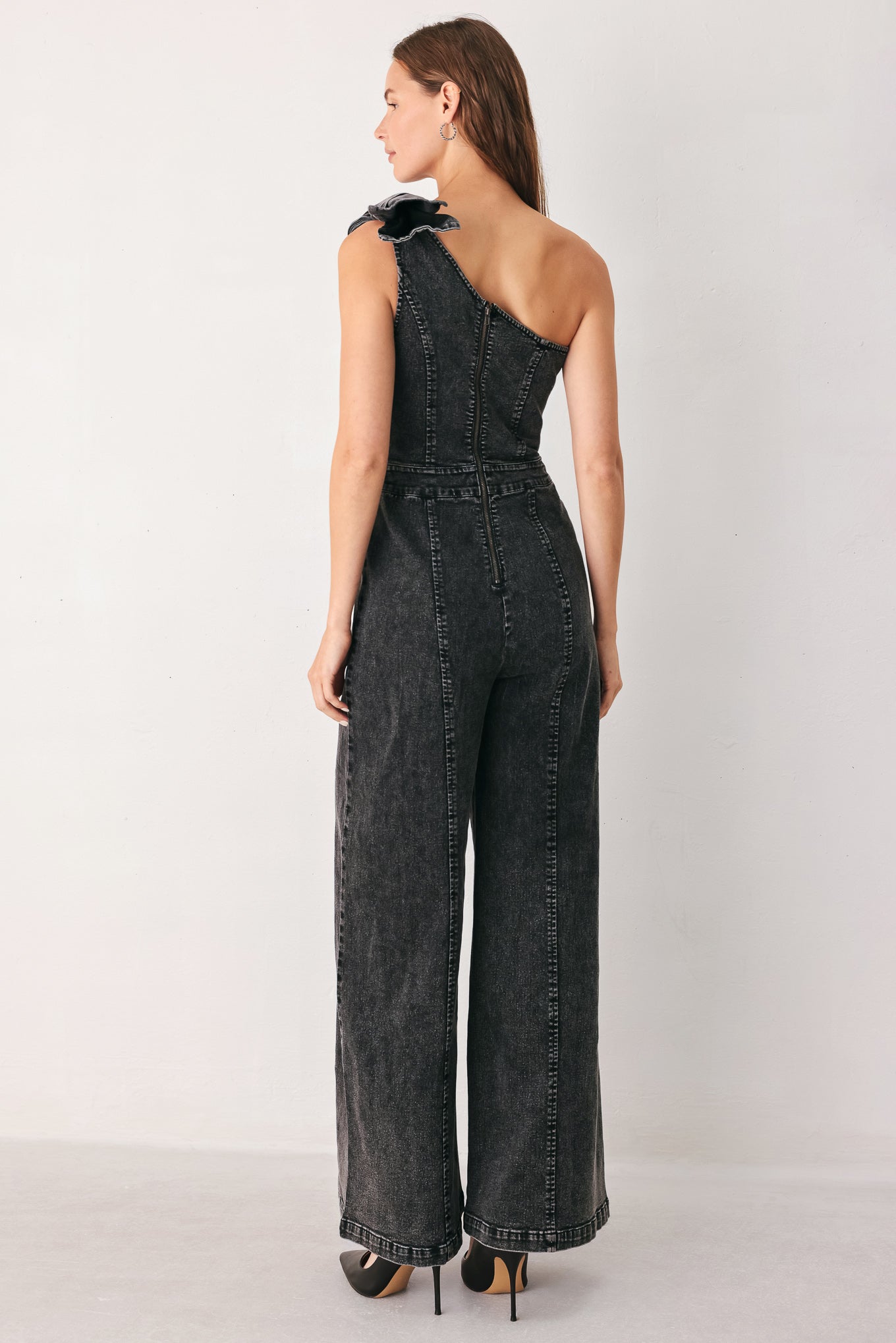 A woman wearing a dark gray washed denim one-shoulder jumpsuit with a wide-leg pant leg and a ruffled bow detail on the shoulder | FREEMARKET