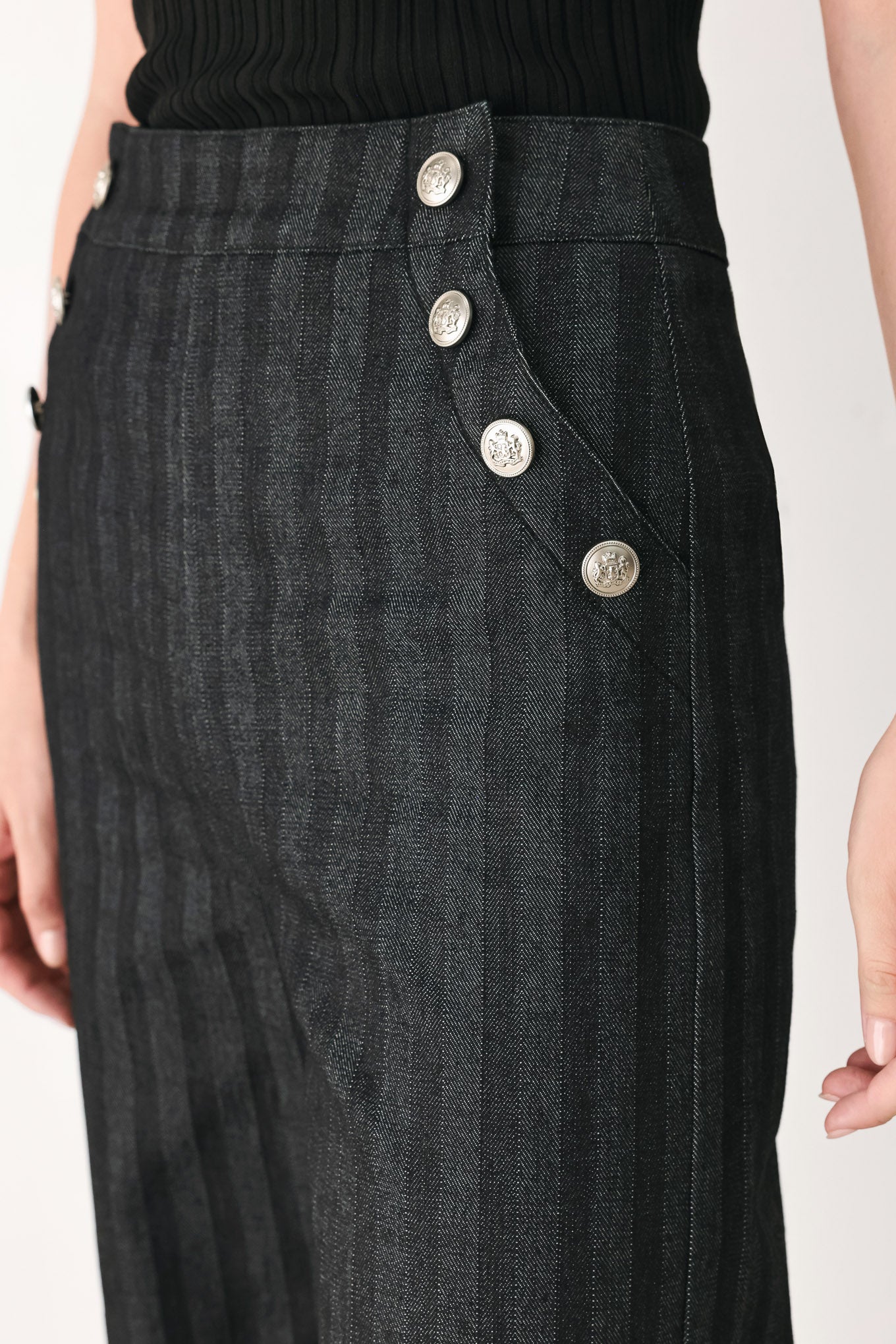 A model wearing a pair of high-waisted, wide-leg trousers in a dark gray and black pinstripe pattern, featuring decorative silver buttons on the front waistband | FREEMARKET