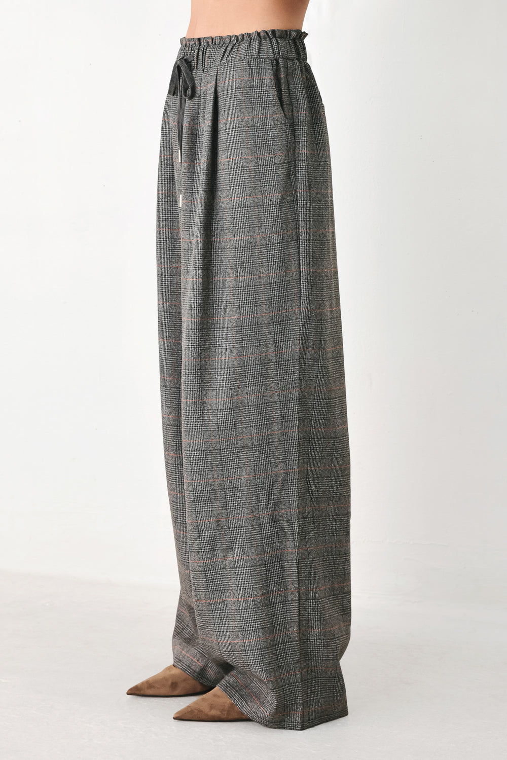 A person wearing loose, wide-leg plaid trousers in dark gray with subtle brown and beige lines, featuring an elastic drawstring waistband | FREEMARKET