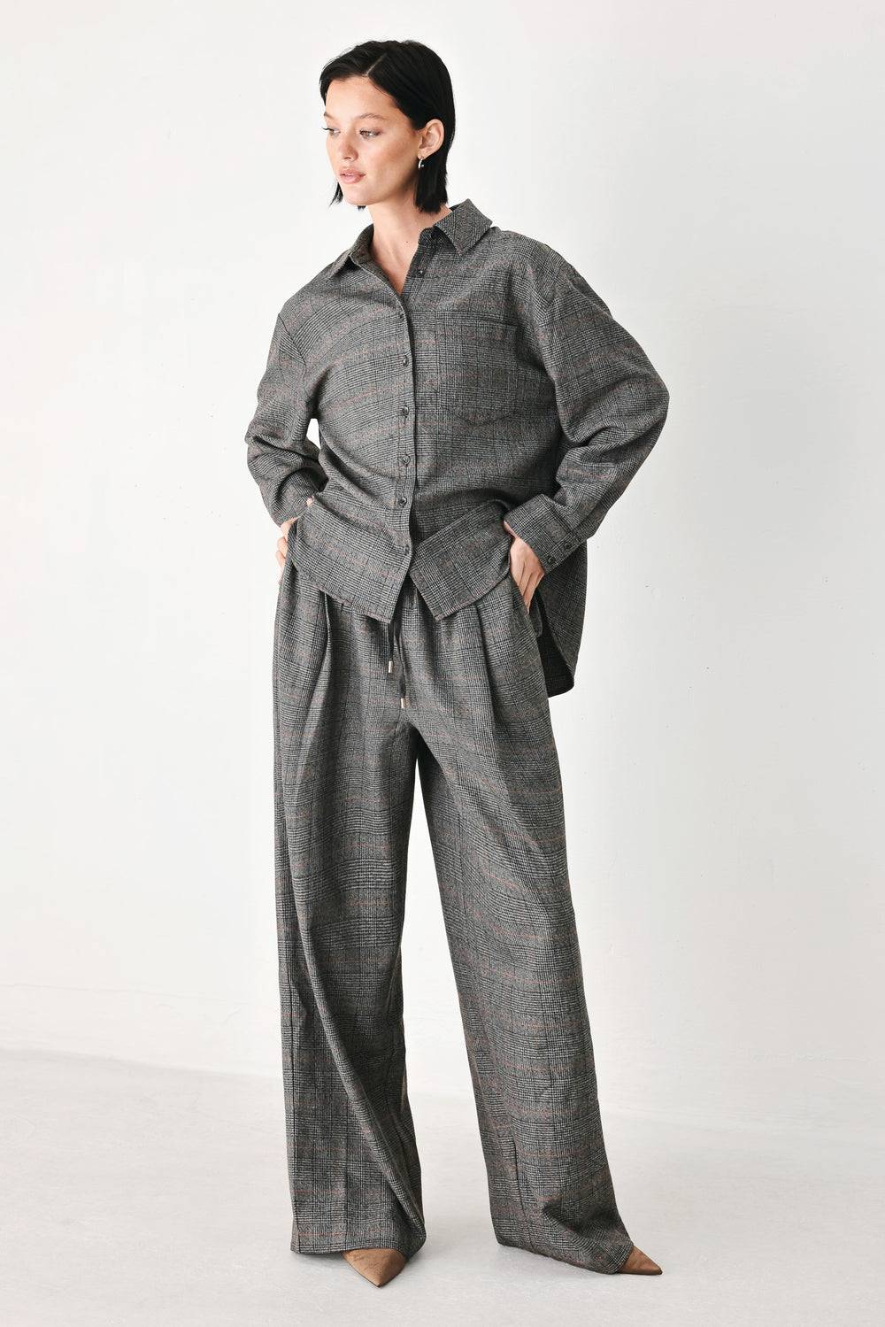 A person wearing loose, wide-leg plaid trousers in dark gray with subtle brown and beige lines, featuring an elastic drawstring waistband | FREEMARKET