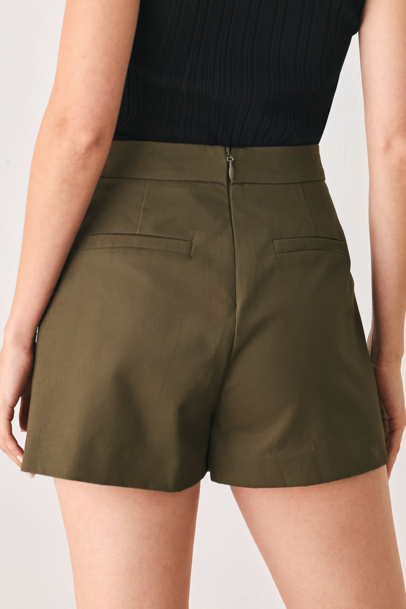 A woman wearing an olive green mini skort with double-breasted silver buttons | FREEMARKET