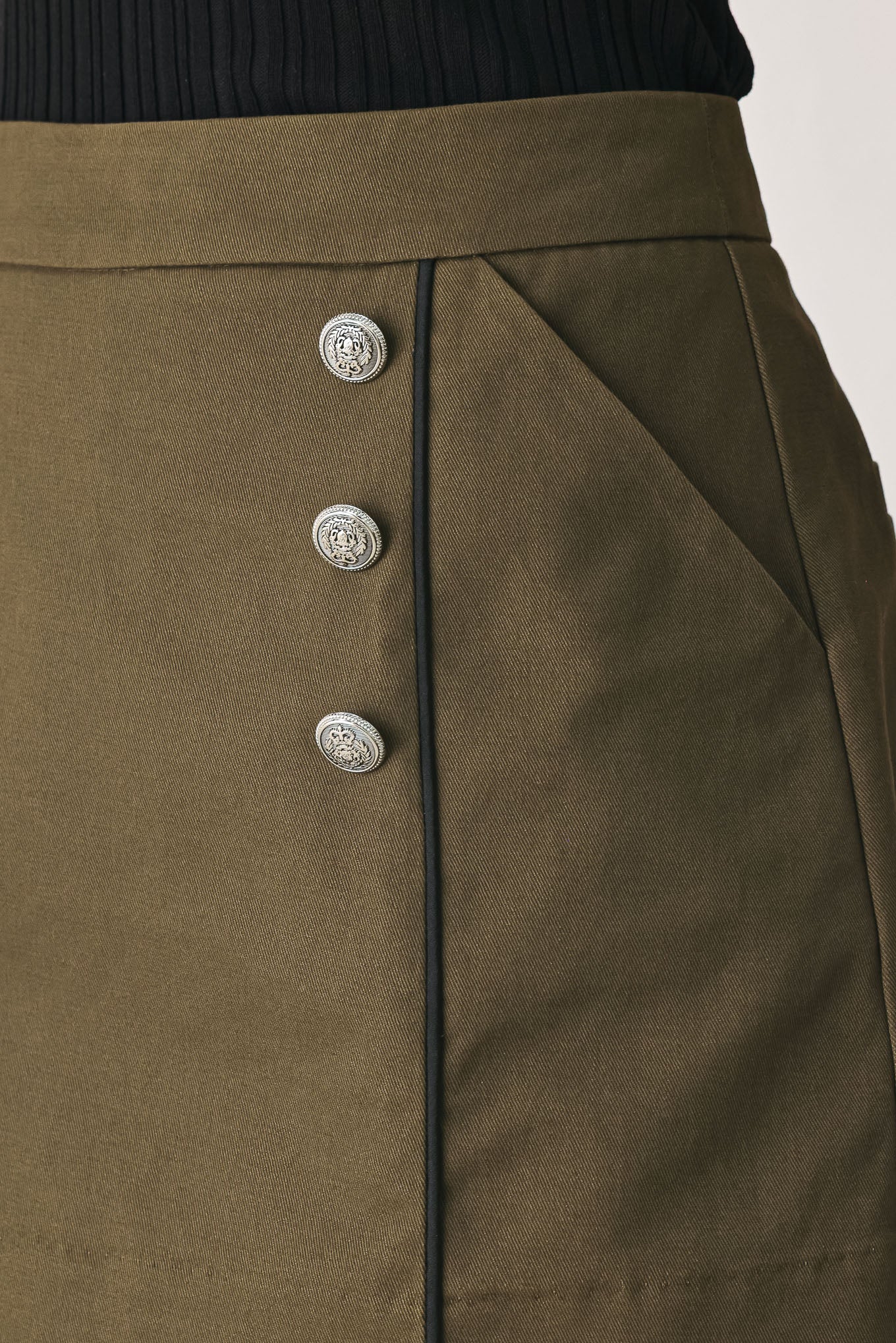 A woman wearing an olive green mini skort with double-breasted silver buttons | FREEMARKET