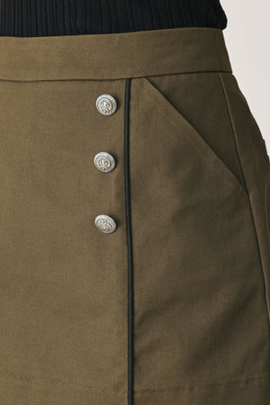 A woman wearing an olive green mini skort with double-breasted silver buttons | FREEMARKET