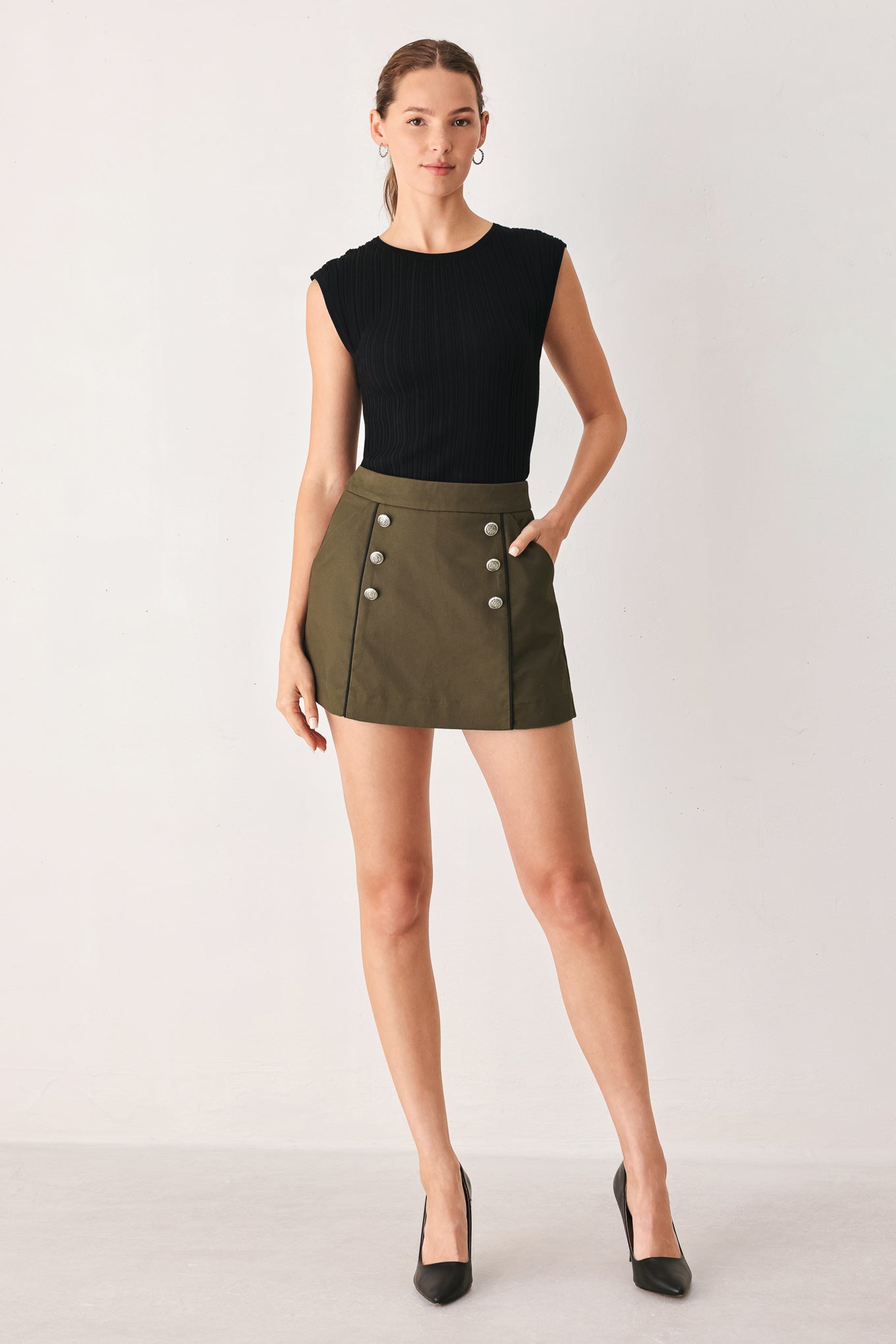 A woman wearing an olive green mini skort with double-breasted silver buttons | FREEMARKET