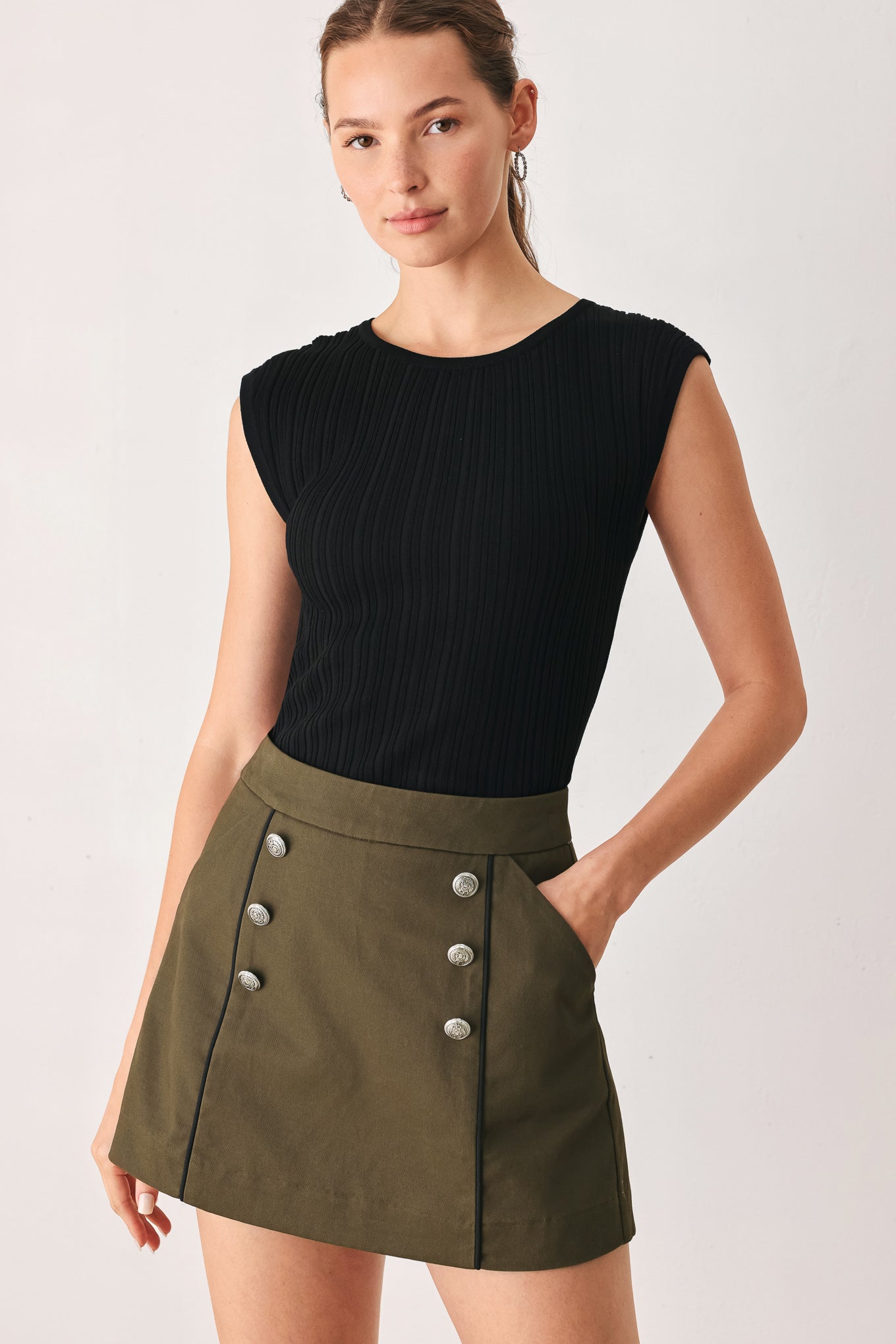 A woman wearing an olive green mini skort with double-breasted silver buttons | FREEMARKET