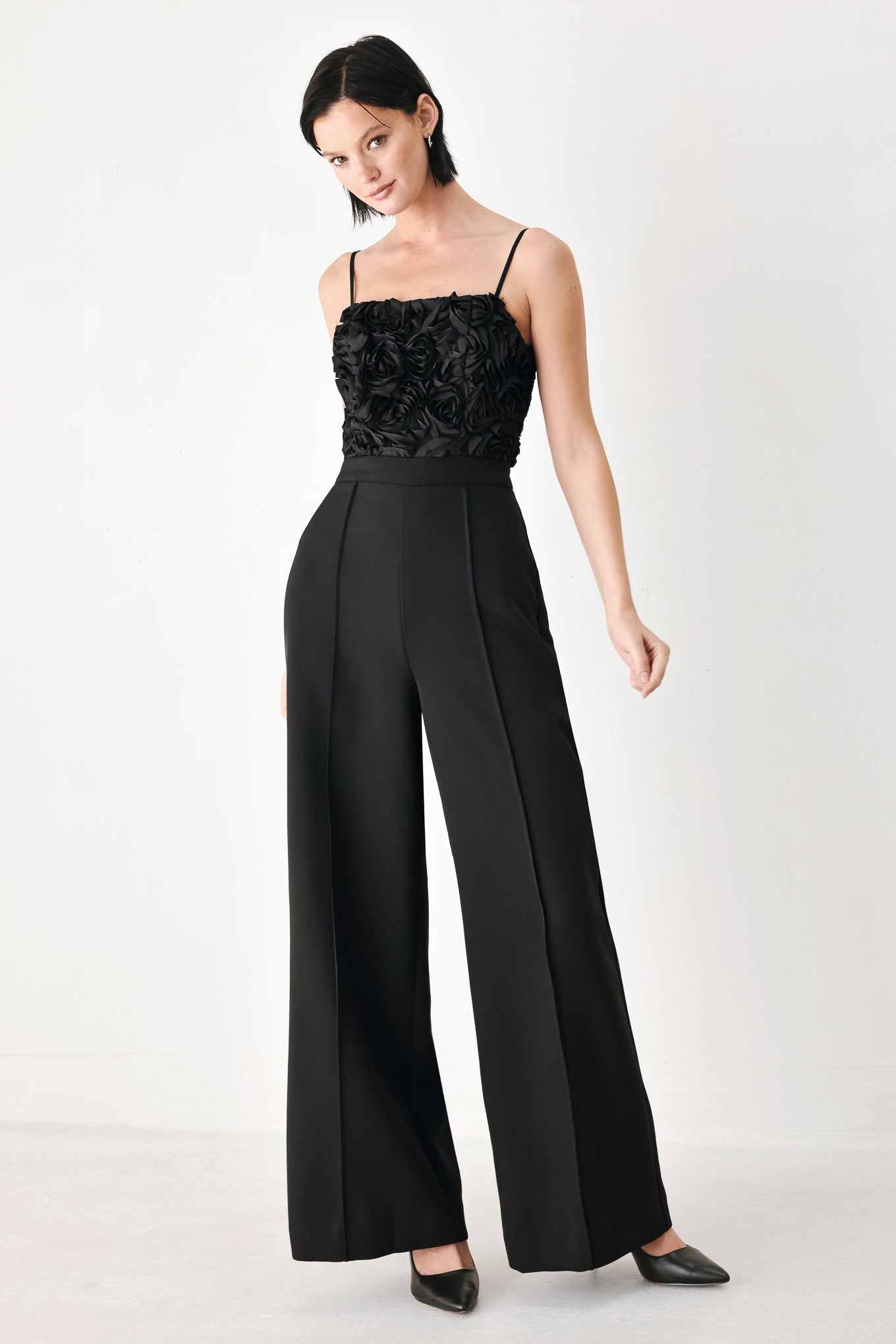 A woman modeling a black sleeveless jumpsuit with a textured floral bodice and wide-leg trousers | FREEMARKET