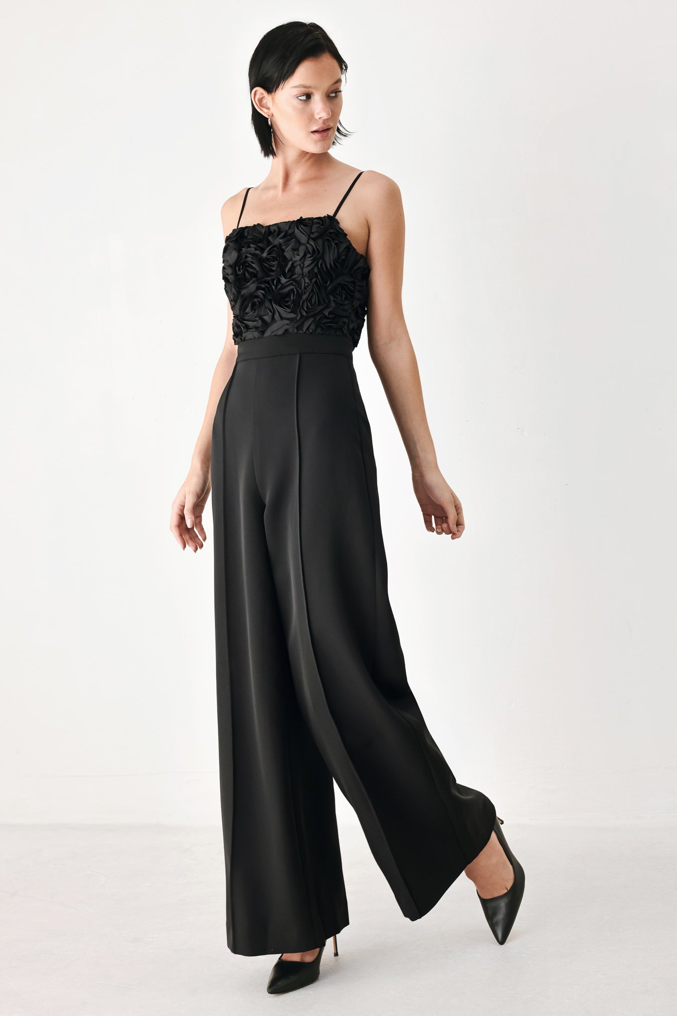 A woman modeling a black sleeveless jumpsuit with a textured floral bodice and wide-leg trousers | FREEMARKET