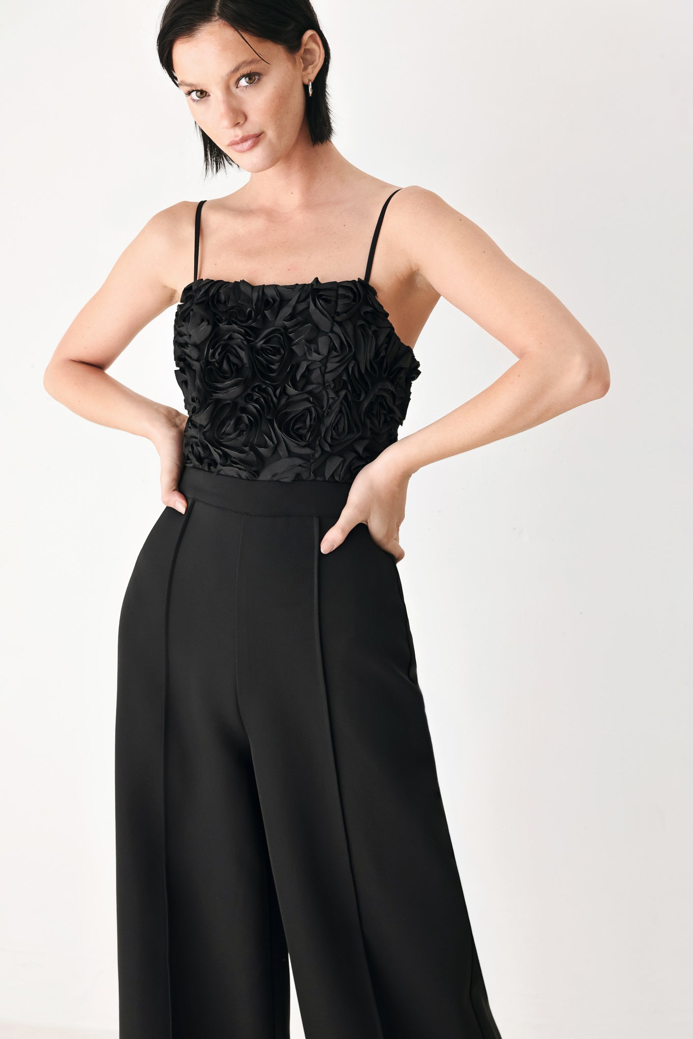 A woman modeling a black sleeveless jumpsuit with a textured floral bodice and wide-leg trousers | FREEMARKET