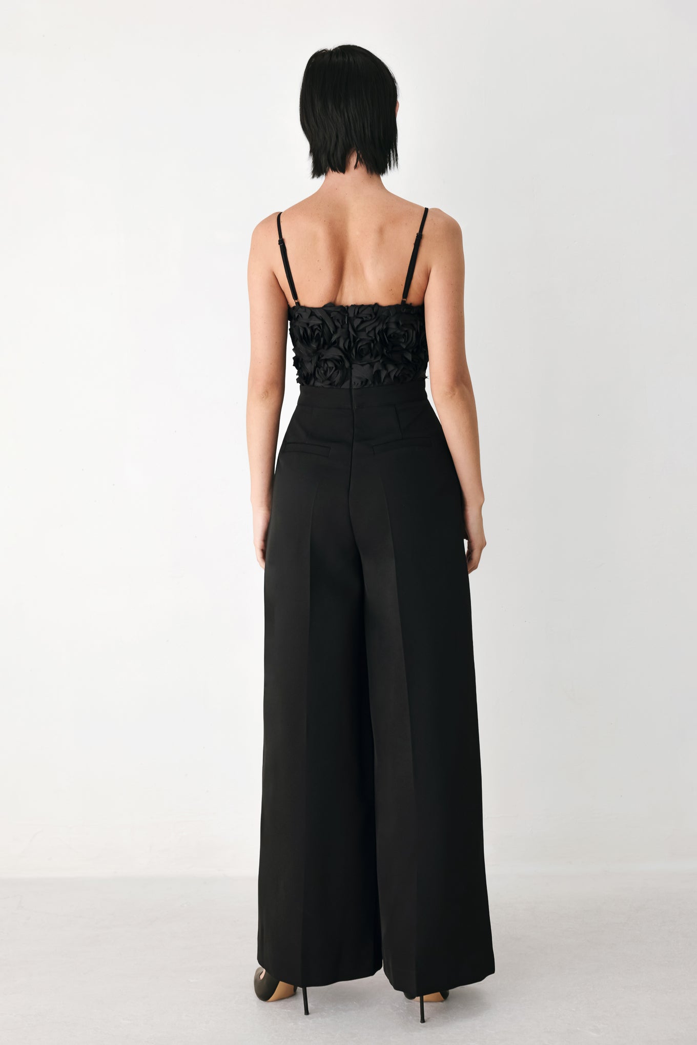 A woman modeling a black sleeveless jumpsuit with a textured floral bodice and wide-leg trousers | FREEMARKET
