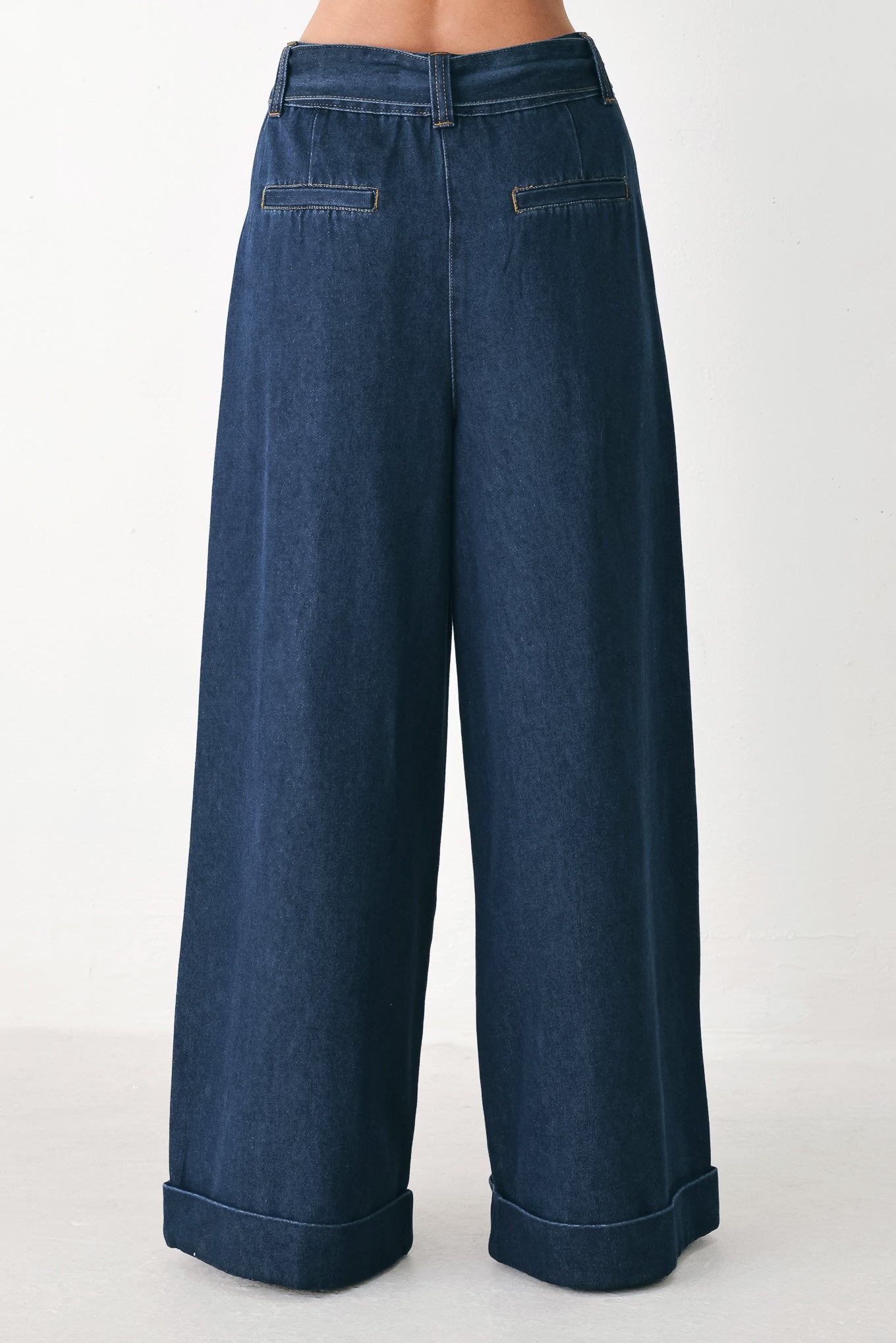 A person wearing dark blue wide-leg denim pants with a rolled cuff and a gold-tone belt buckle | FREEMARKET