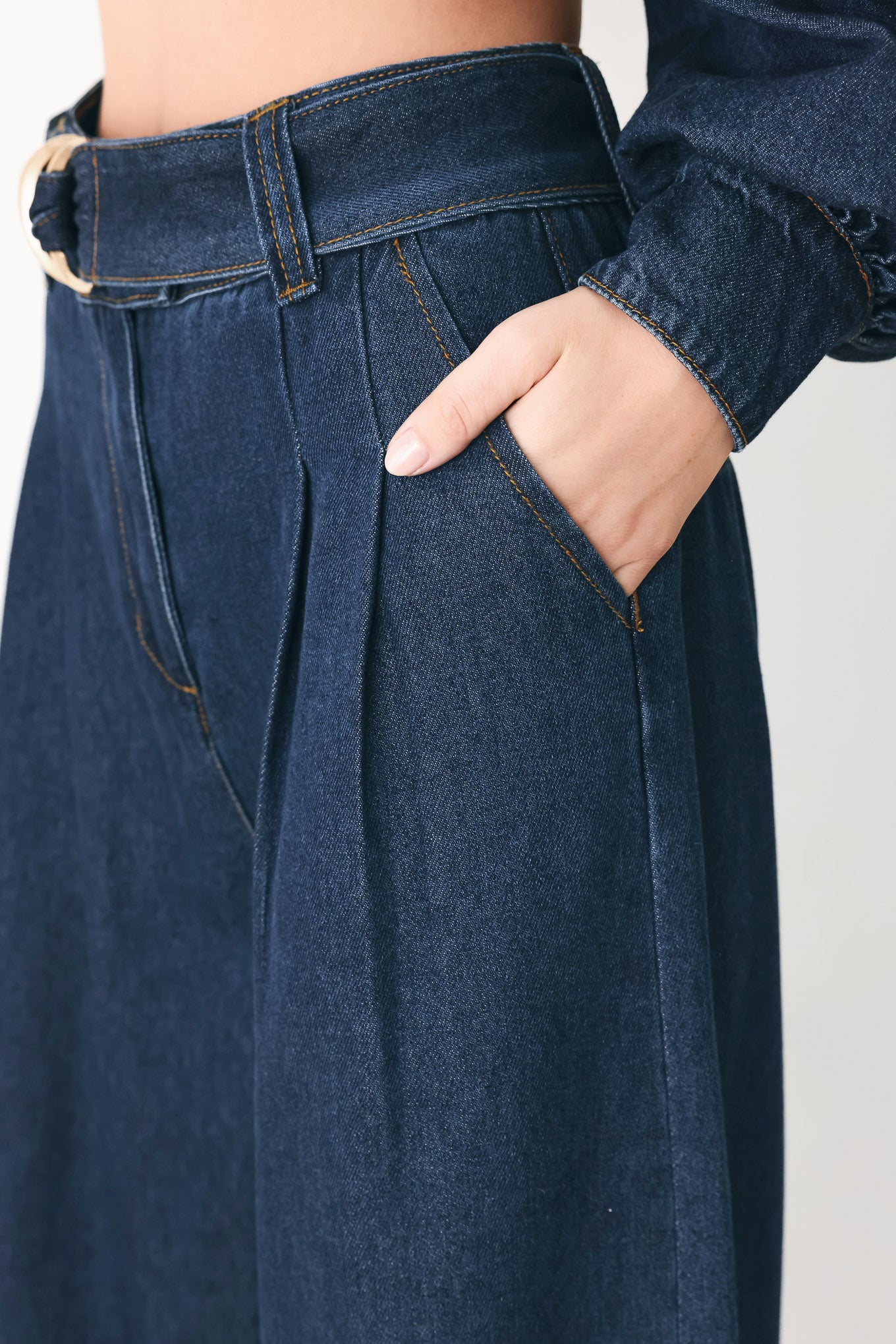 A person wearing dark blue wide-leg denim pants with a rolled cuff and a gold-tone belt buckle | FREEMARKET
