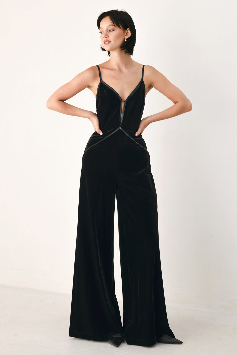 A woman modeling a black velvet wide-leg jumpsuit with thin straps, a plunging neckline | FREEMARKET