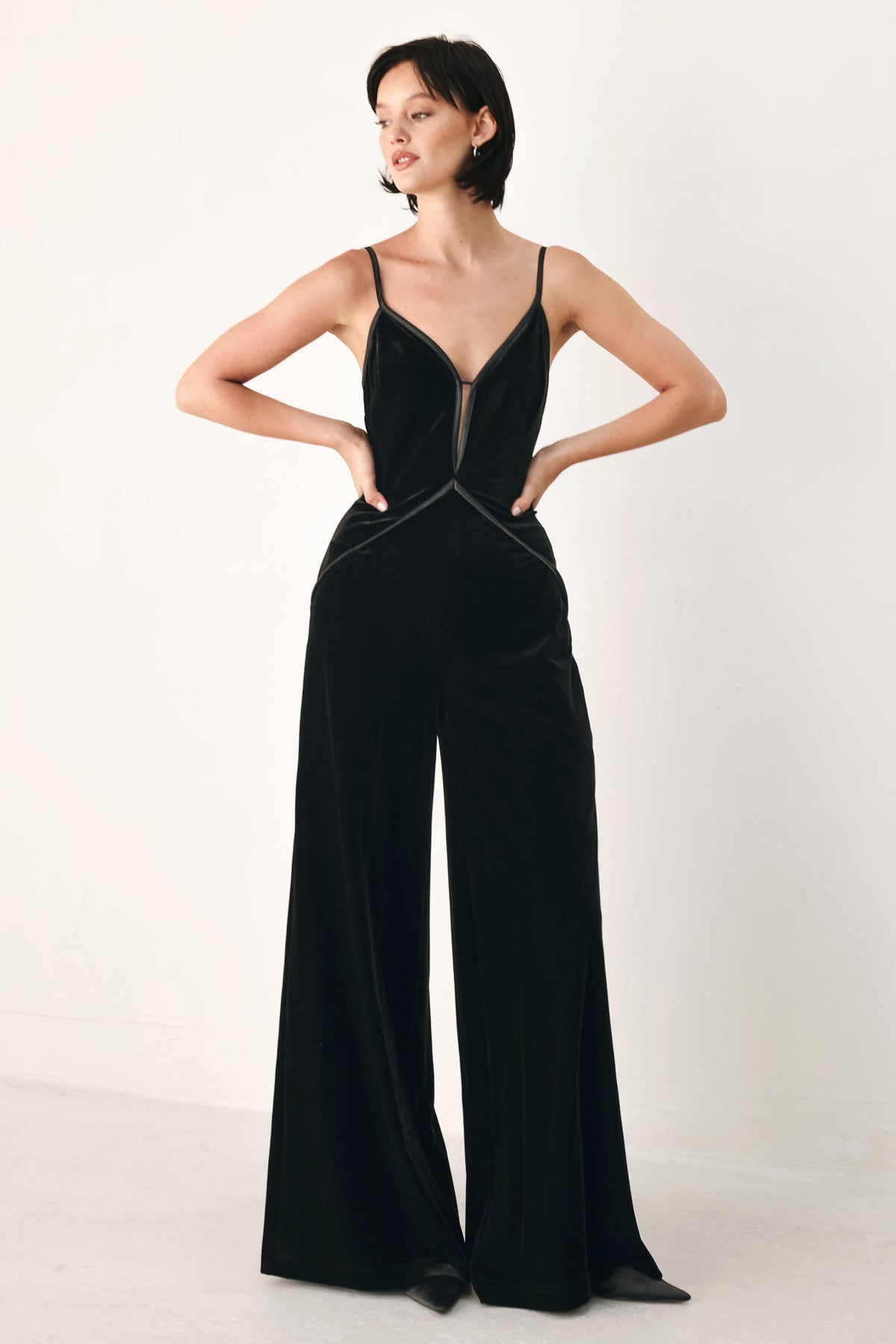 A woman modeling a black velvet wide-leg jumpsuit with thin straps, a plunging neckline | FREEMARKET