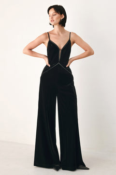 A woman modeling a black velvet wide-leg jumpsuit with thin straps, a plunging neckline | FREEMARKET