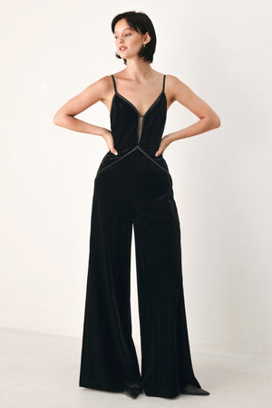A woman modeling a black velvet wide-leg jumpsuit with thin straps, a plunging neckline | FREEMARKET