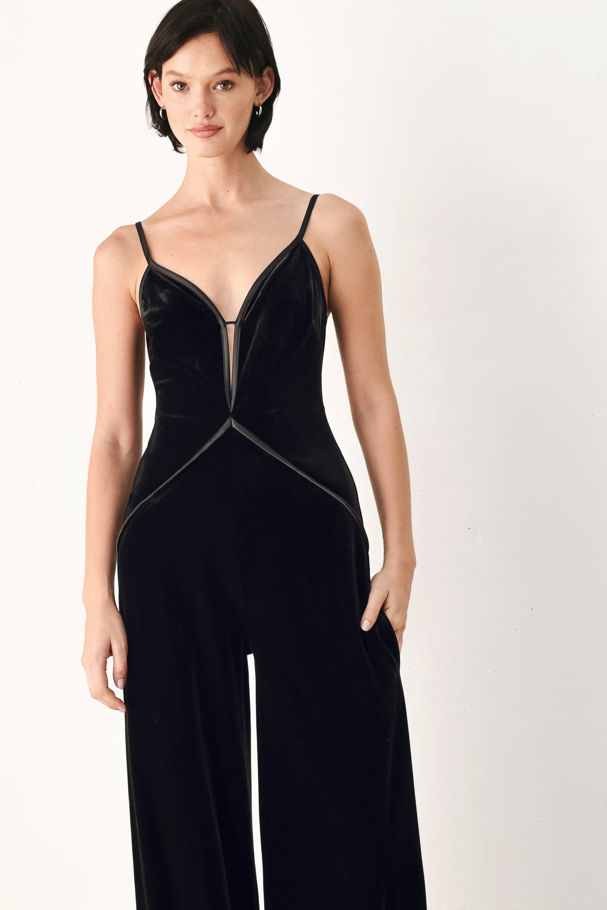 A woman modeling a black velvet wide-leg jumpsuit with thin straps, a plunging neckline | FREEMARKET