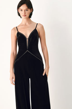 A woman modeling a black velvet wide-leg jumpsuit with thin straps, a plunging neckline | FREEMARKET