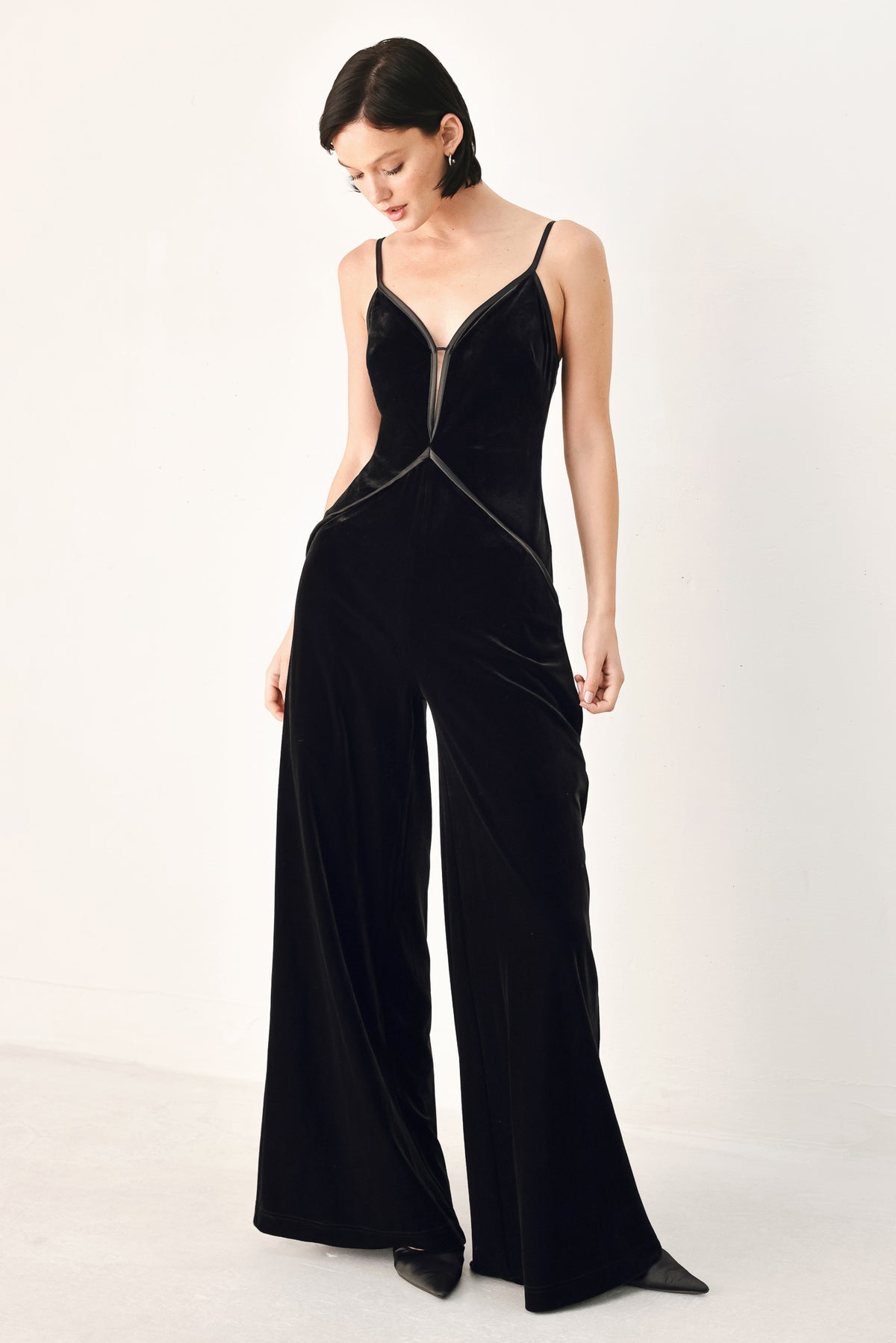 A woman modeling a black velvet wide-leg jumpsuit with thin straps, a plunging neckline | FREEMARKET