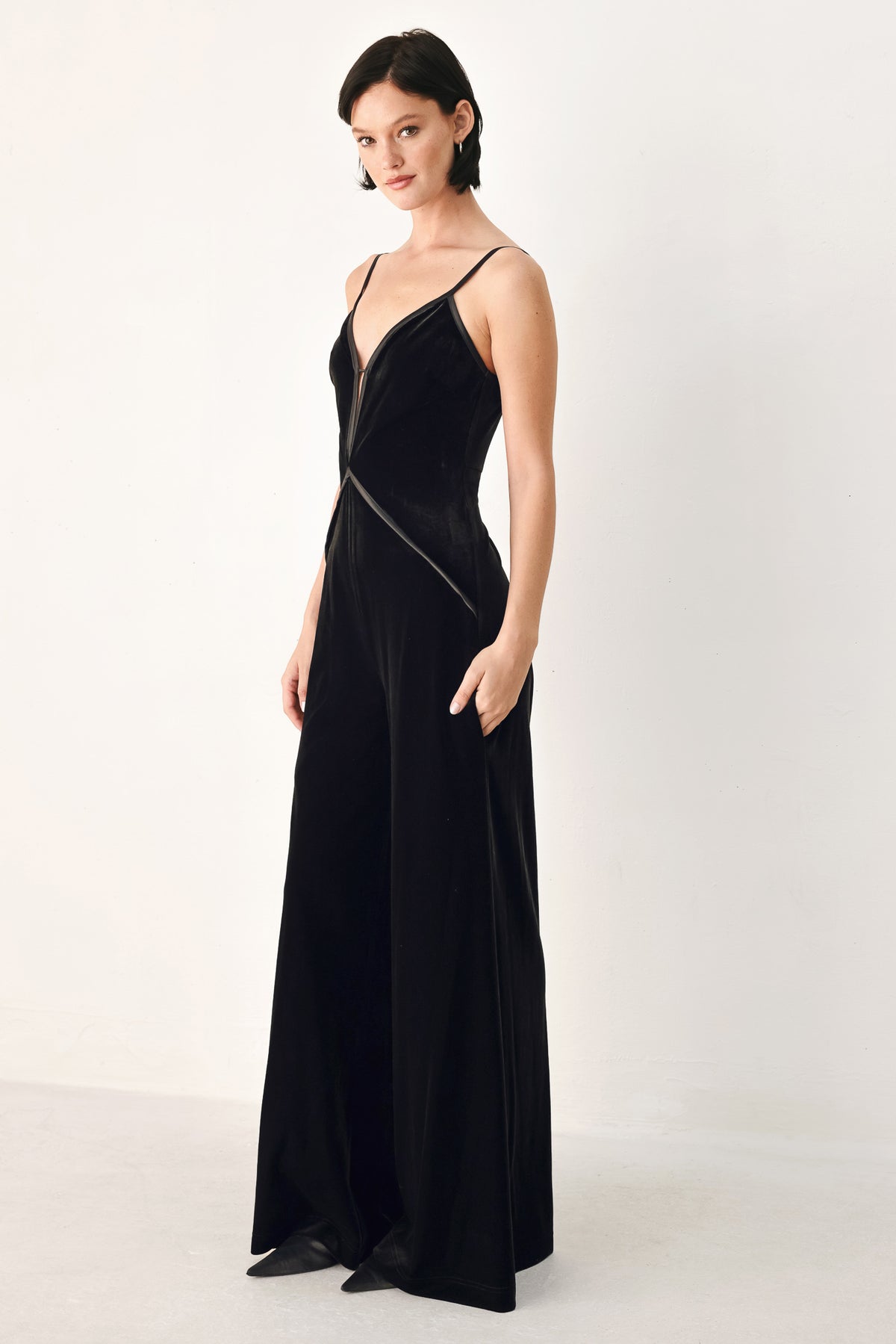 A woman modeling a black velvet wide-leg jumpsuit with thin straps, a plunging neckline | FREEMARKET