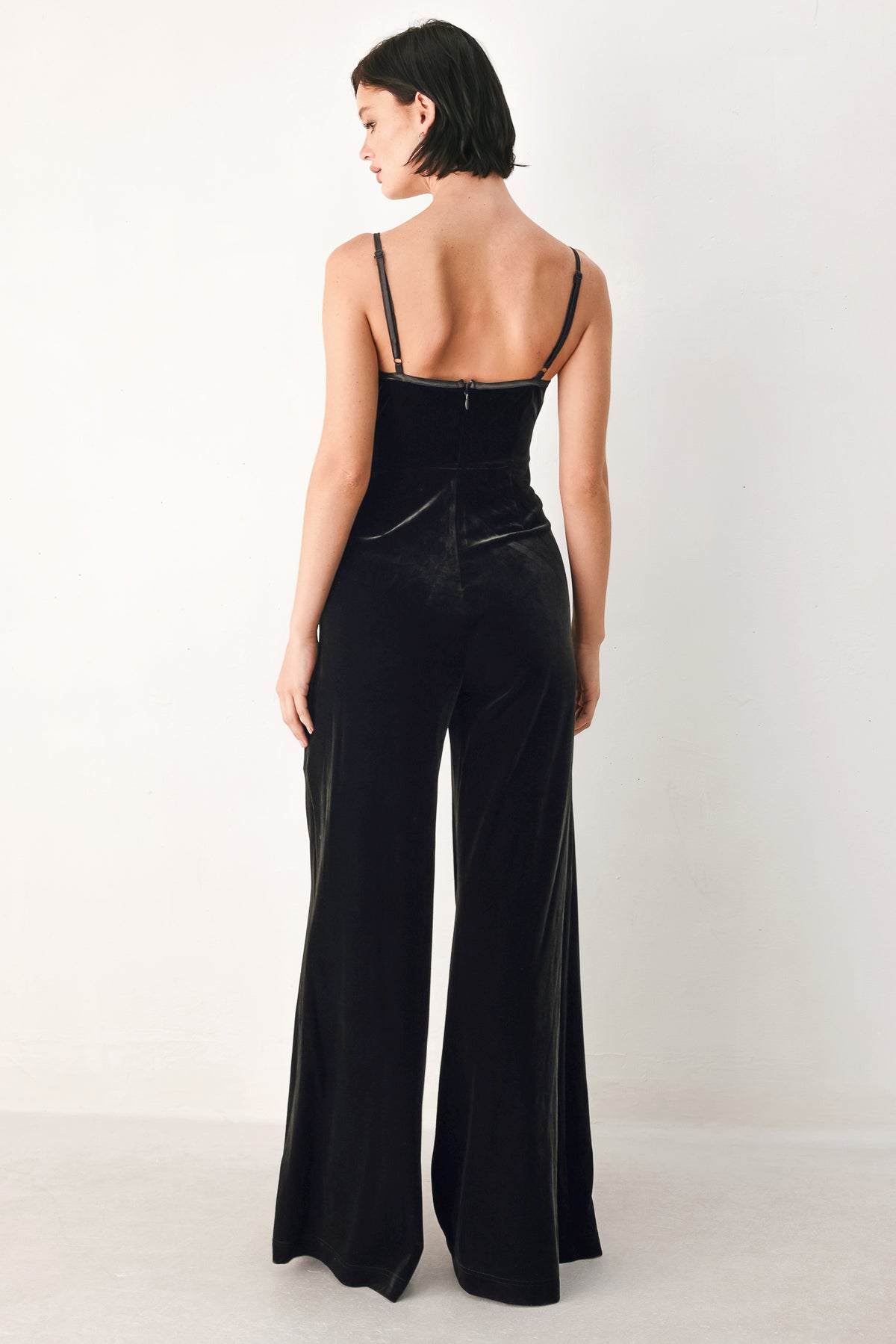 A woman modeling a black velvet wide-leg jumpsuit with thin straps, a plunging neckline | FREEMARKET