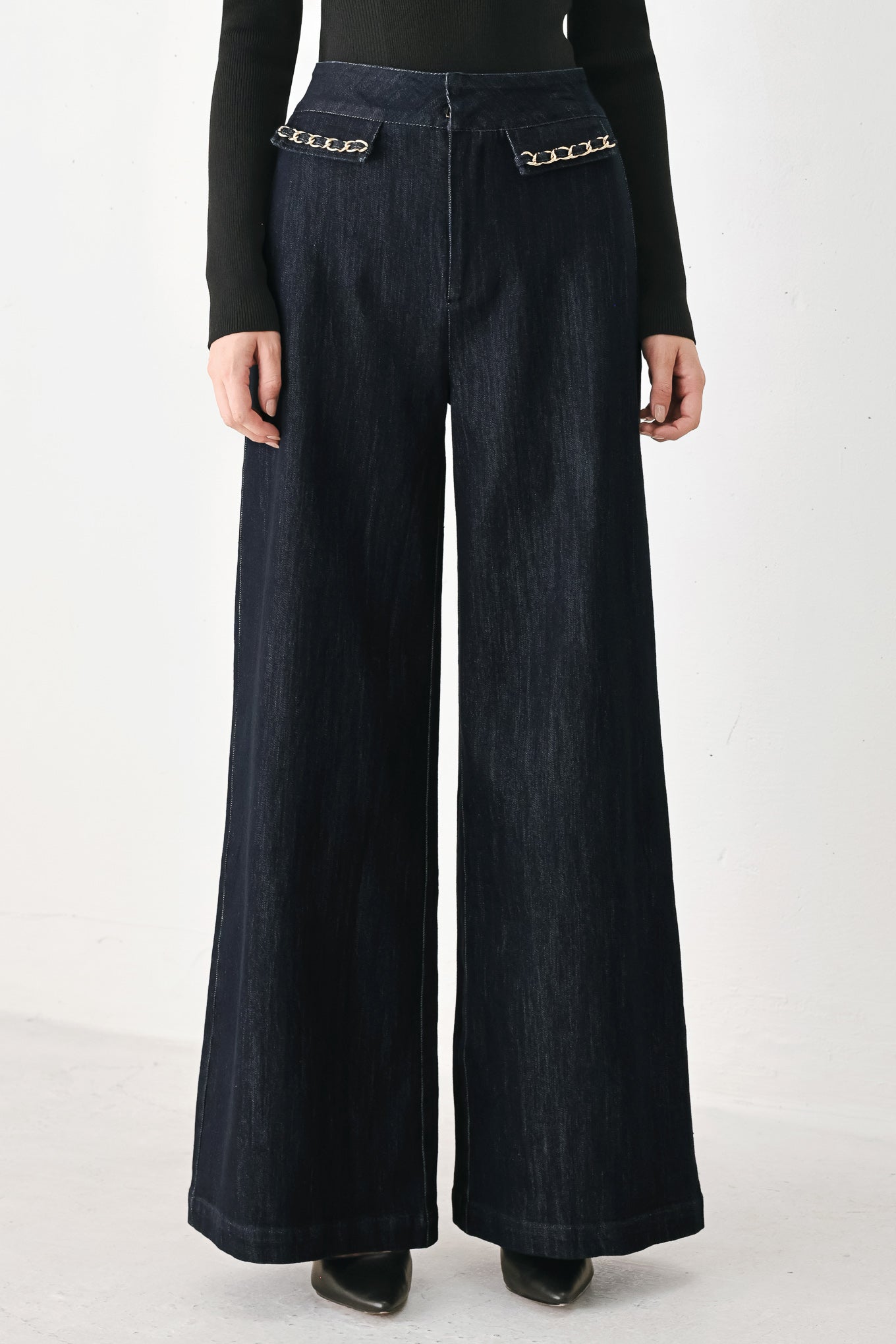 A model wearing dark indigo wide-leg denim jeans with gold chain embellishments on the front pockets | FREEMARKET