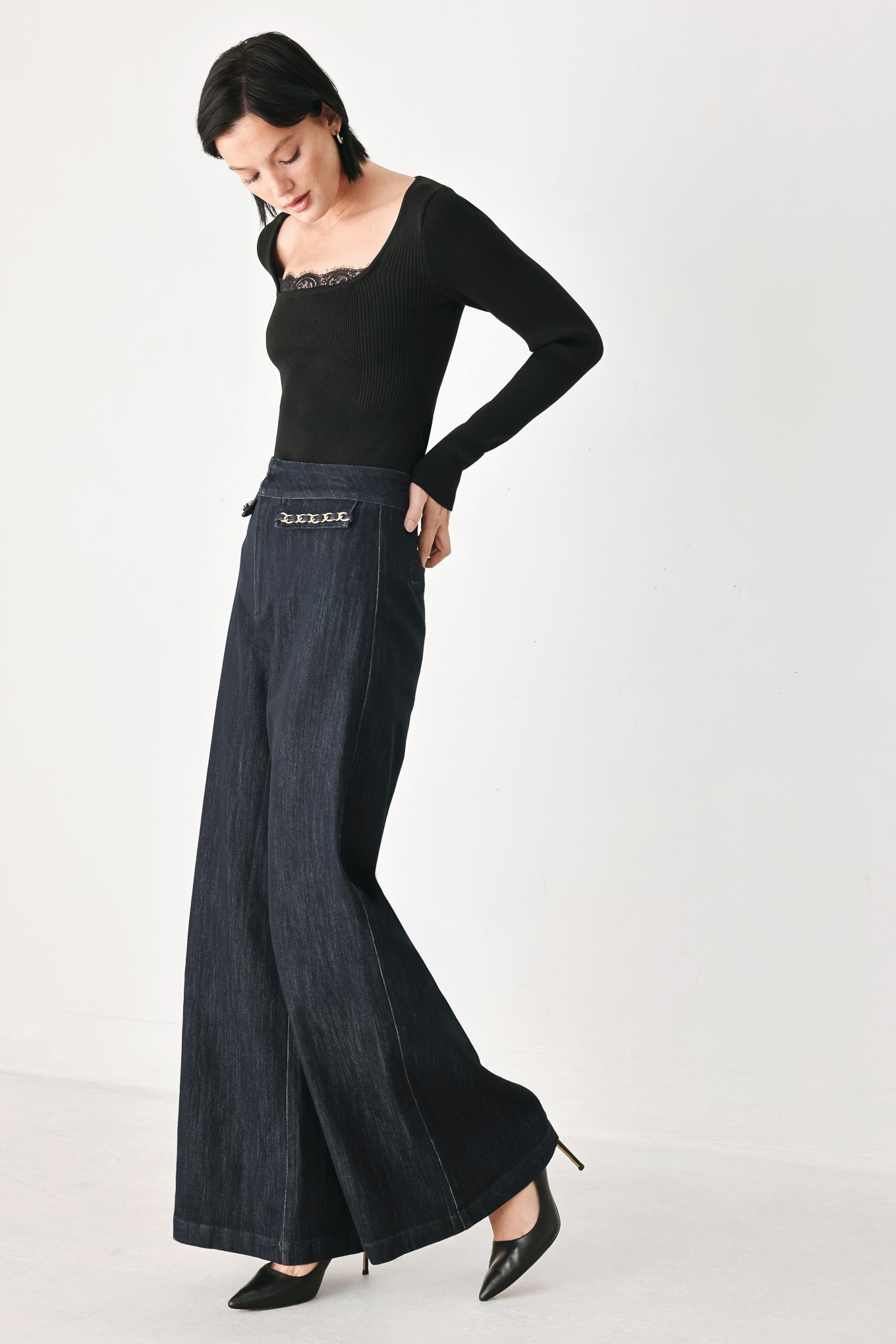 A model wearing dark indigo wide-leg denim jeans with gold chain embellishments on the front pockets | FREEMARKET