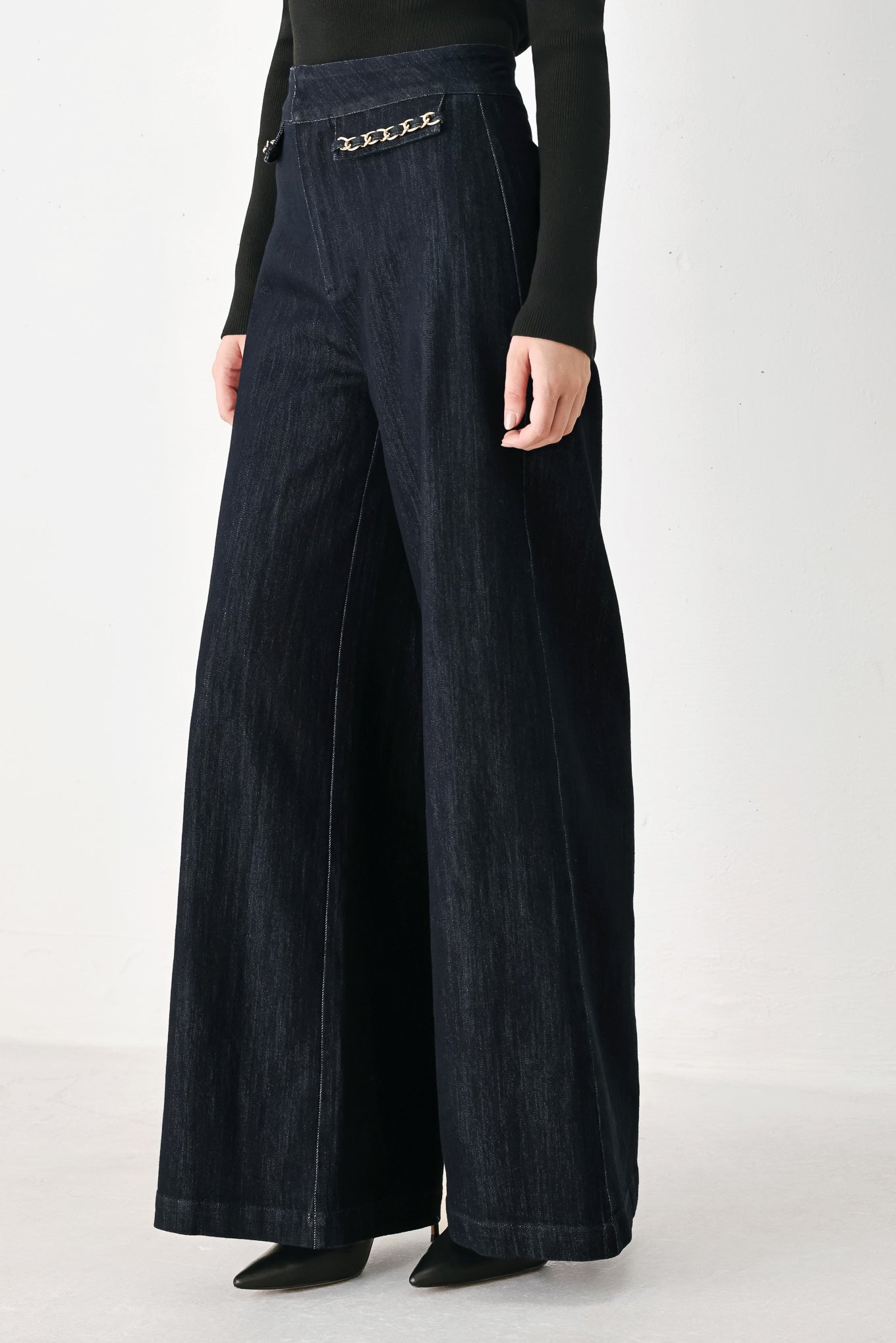 A model wearing dark indigo wide-leg denim jeans with gold chain embellishments on the front pockets | FREEMARKET