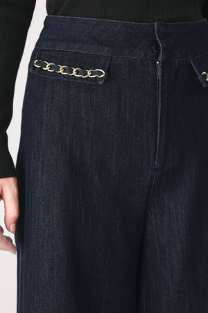 A model wearing dark indigo wide-leg denim jeans with gold chain embellishments on the front pockets | FREEMARKET
