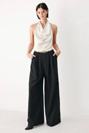 A model wearing a sleeveless jumpsuit with draped white top and black wide-leg trousers, and a thin gold belt with a round buckle | FREEMARKET