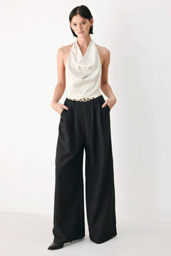 A model wearing a sleeveless jumpsuit with draped white top and black wide-leg trousers, and a thin gold belt with a round buckle | FREEMARKET