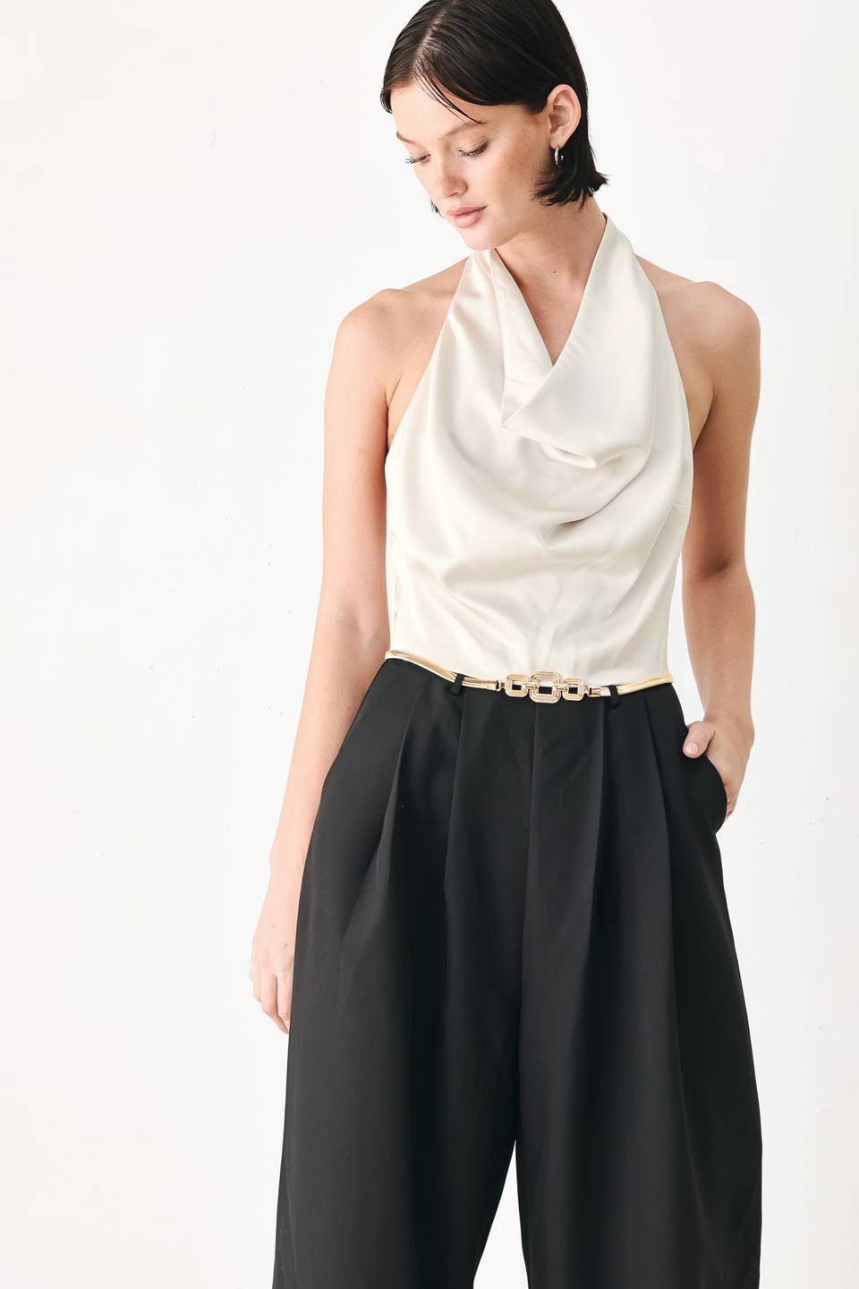 A model wearing a sleeveless jumpsuit with draped white top and black wide-leg trousers, and a thin gold belt with a round buckle | FREEMARKET