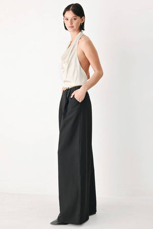 A model wearing a sleeveless jumpsuit with draped white top and black wide-leg trousers, and a thin gold belt with a round buckle | FREEMARKET