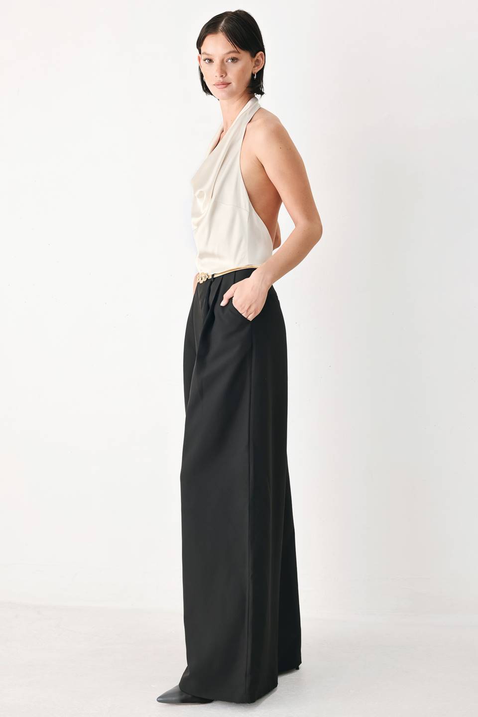 A model wearing a sleeveless jumpsuit with draped white top and black wide-leg trousers, and a thin gold belt with a round buckle | FREEMARKET