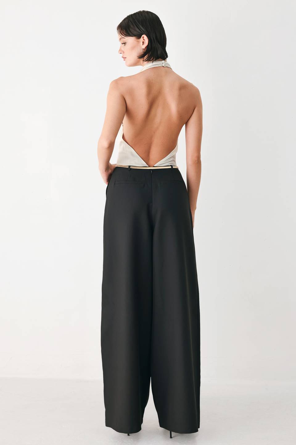 A model wearing a sleeveless jumpsuit with draped white top and black wide-leg trousers, and a thin gold belt with a round buckle | FREEMARKET