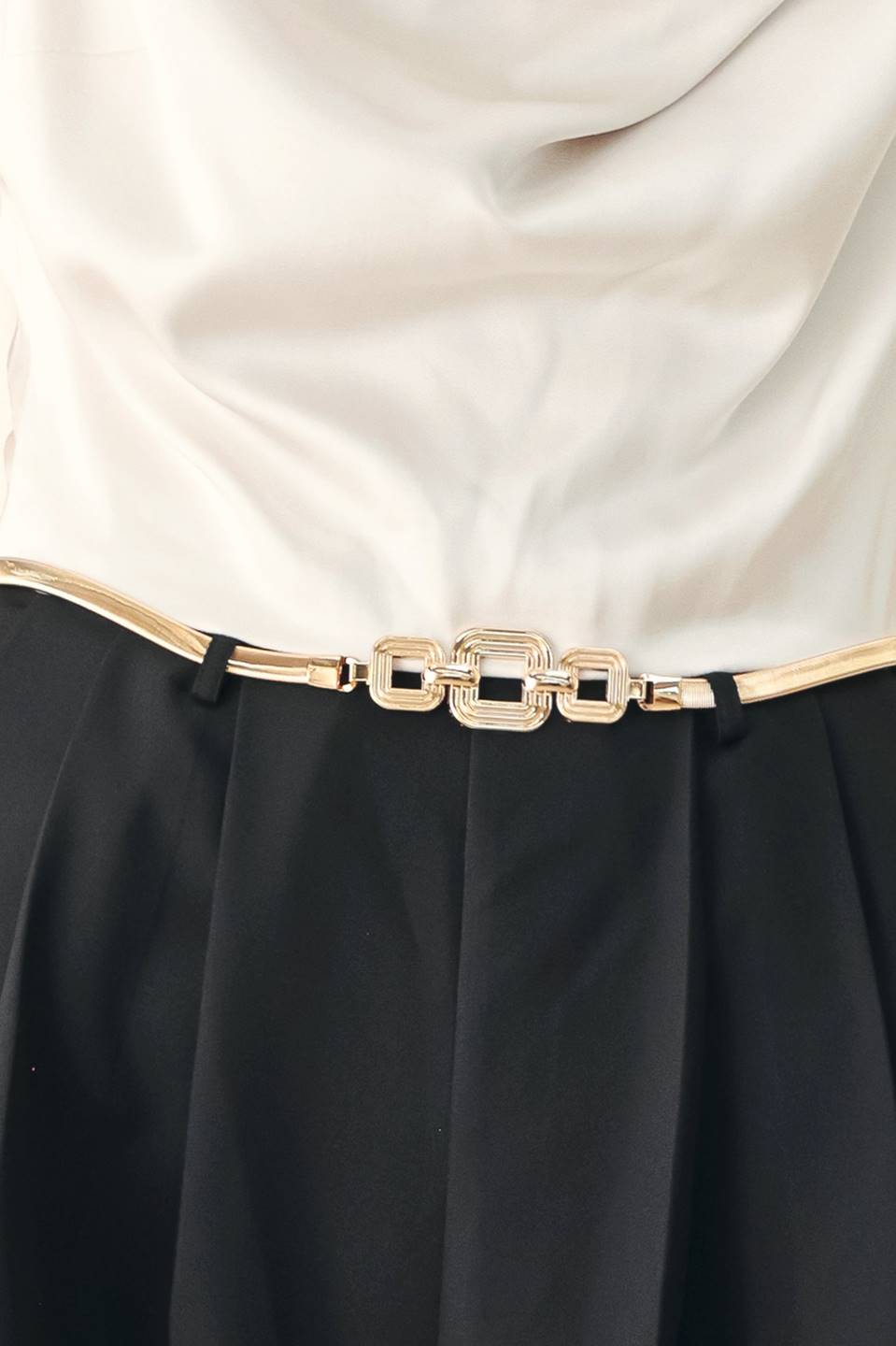 A model wearing a sleeveless jumpsuit with draped white top and black wide-leg trousers, and a thin gold belt with a round buckle | FREEMARKET