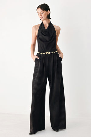 A model wearing a black pleated halter-neck jumpsuit with wide legs, pinstripes, and a gold chain belt | FREEMARKET