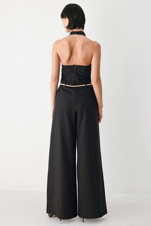 A model wearing a black pleated halter-neck jumpsuit with wide legs, pinstripes, and a gold chain belt | FREEMARKET