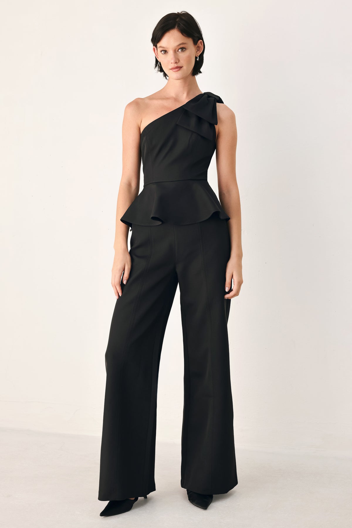 A model wearing a black one-shoulder jumpsuit with a ruffled bodice and wide-leg trousers | FREEMARKET