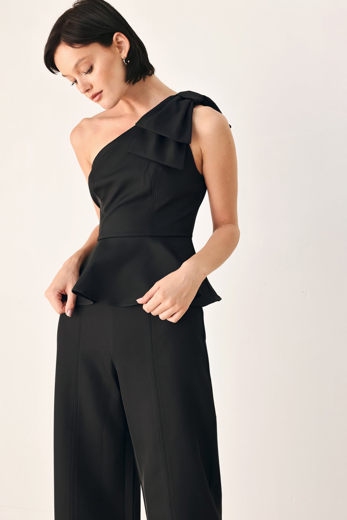 A model wearing a black one-shoulder jumpsuit with a ruffled bodice and wide-leg trousers | FREEMARKET