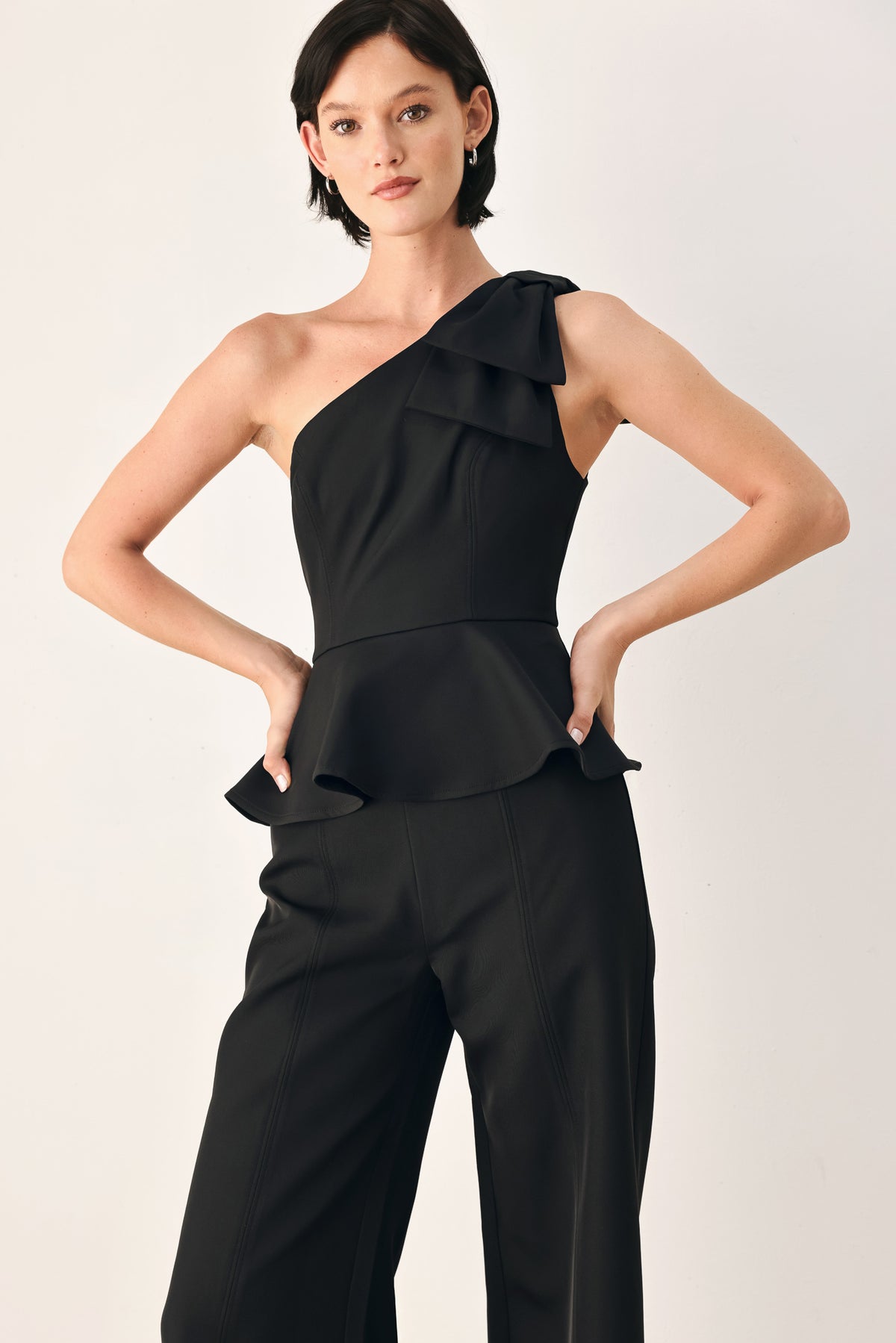 A model wearing a black one-shoulder jumpsuit with a ruffled bodice and wide-leg trousers | FREEMARKET