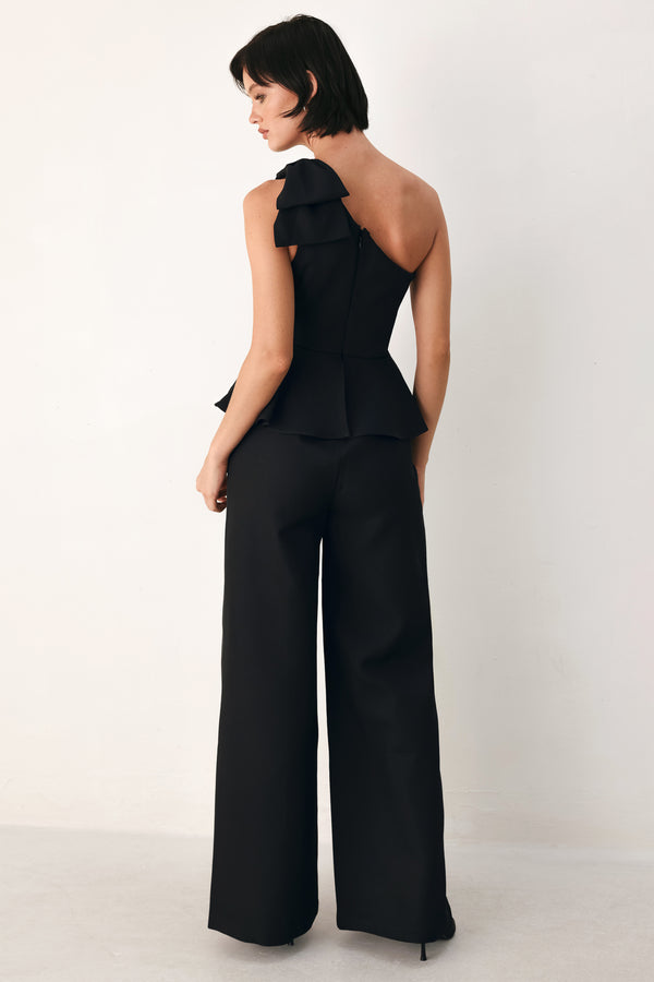 A model wearing a black one-shoulder jumpsuit with a ruffled bodice and wide-leg trousers | FREEMARKET