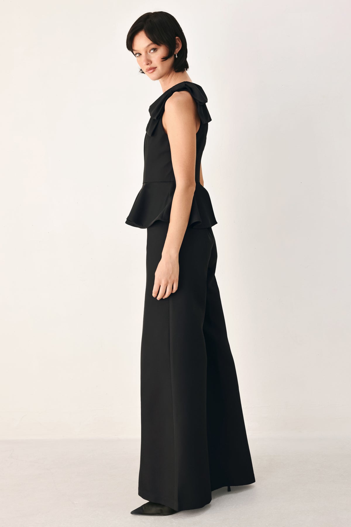 A model wearing a black one-shoulder jumpsuit with a ruffled bodice and wide-leg trousers | FREEMARKET
