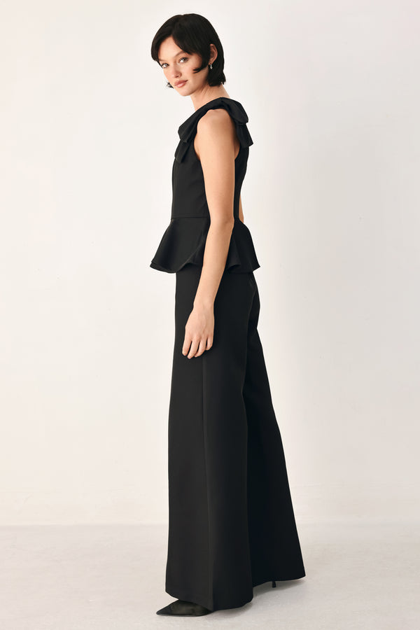 A model wearing a black one-shoulder jumpsuit with a ruffled bodice and wide-leg trousers | FREEMARKET