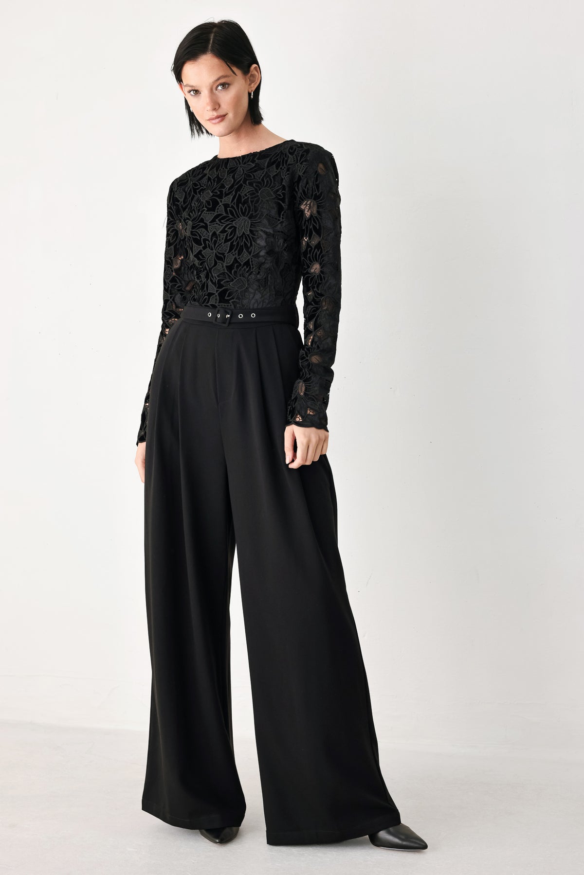 A woman modeling a black long-sleeve jumpsuit with a lace bodice and wide-leg trousers | FREEMARKET
