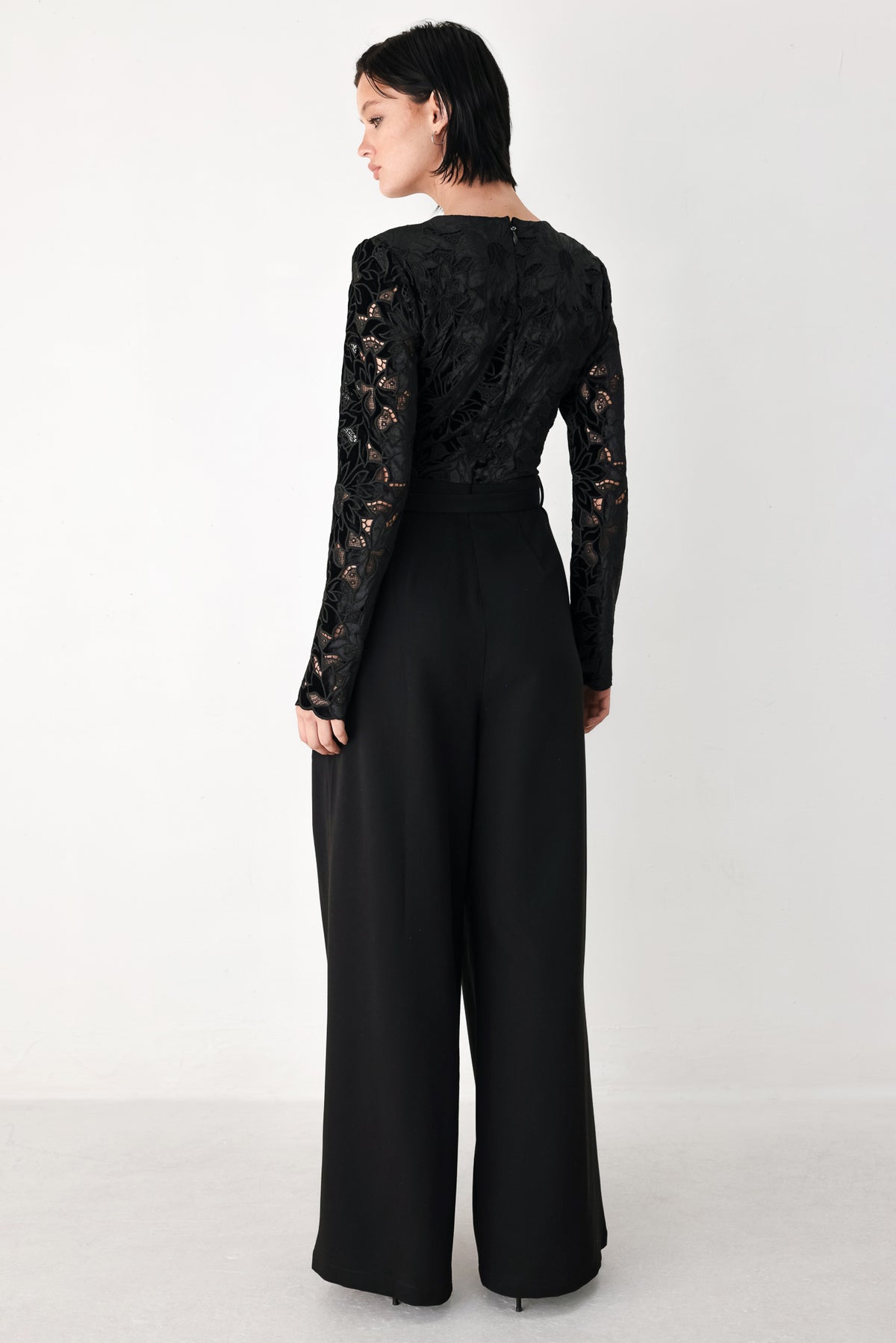 A woman modeling a black long-sleeve jumpsuit with a lace bodice and wide-leg trousers | FREEMARKET