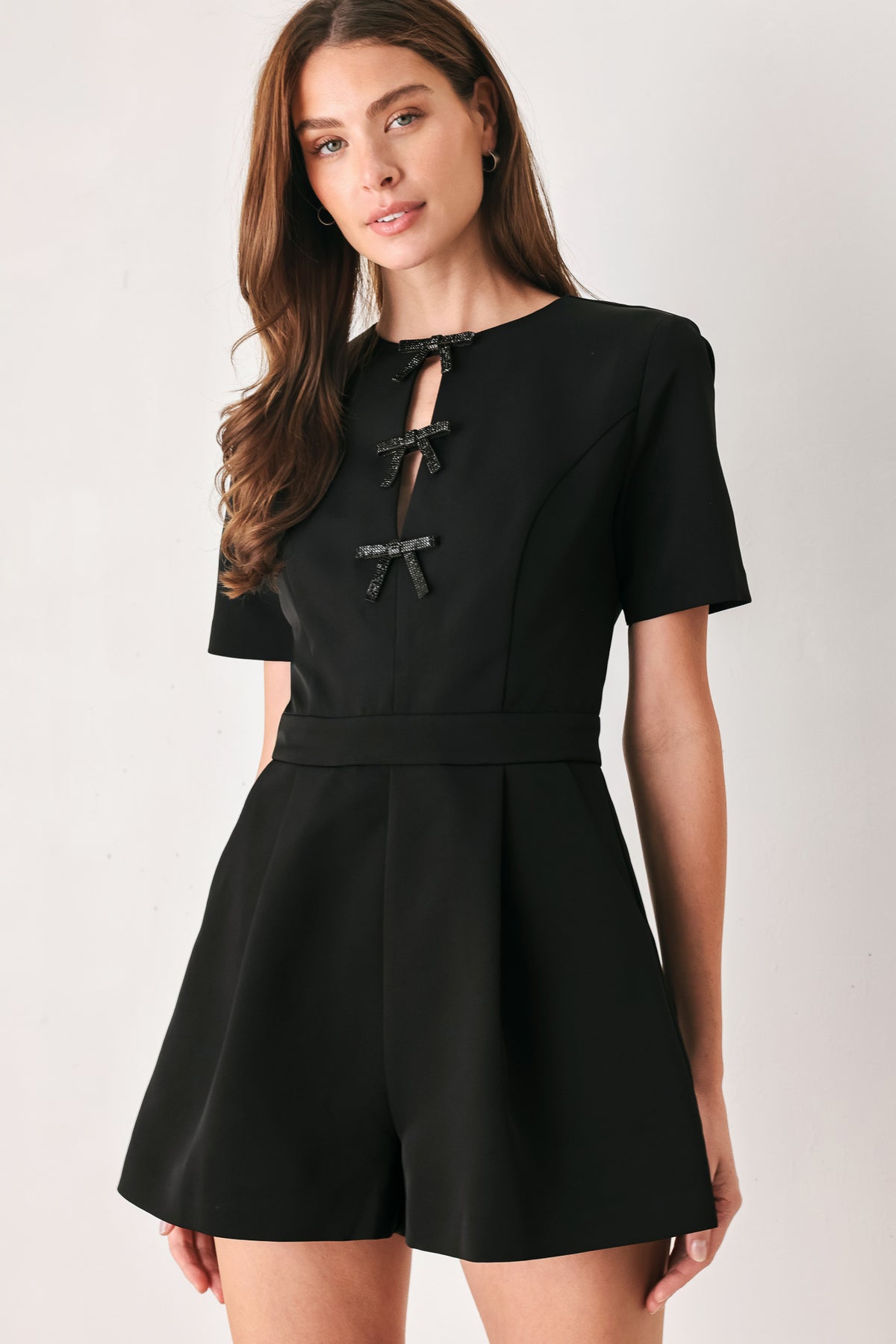 Woman wearing a black short sleeve romper with front keyhole and small embellished bows and pockets | FREEMARKET
