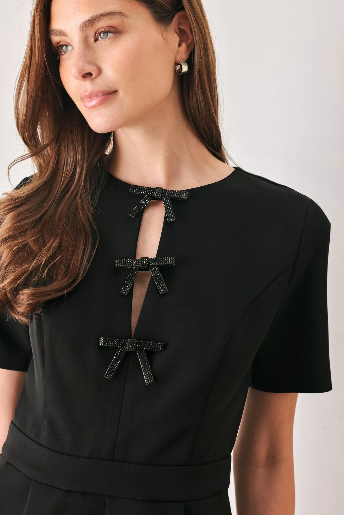 Woman wearing a black short sleeve romper with front keyhole and small embellished bows and pockets | FREEMARKET