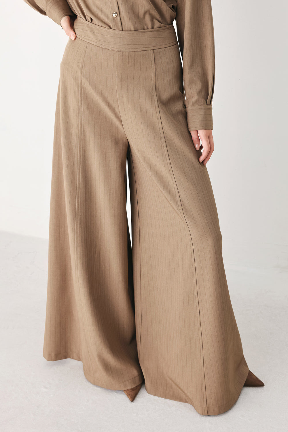 A person wearing high-waisted, wide-leg trousers in a warm taupe-brown color | FREEMARKET